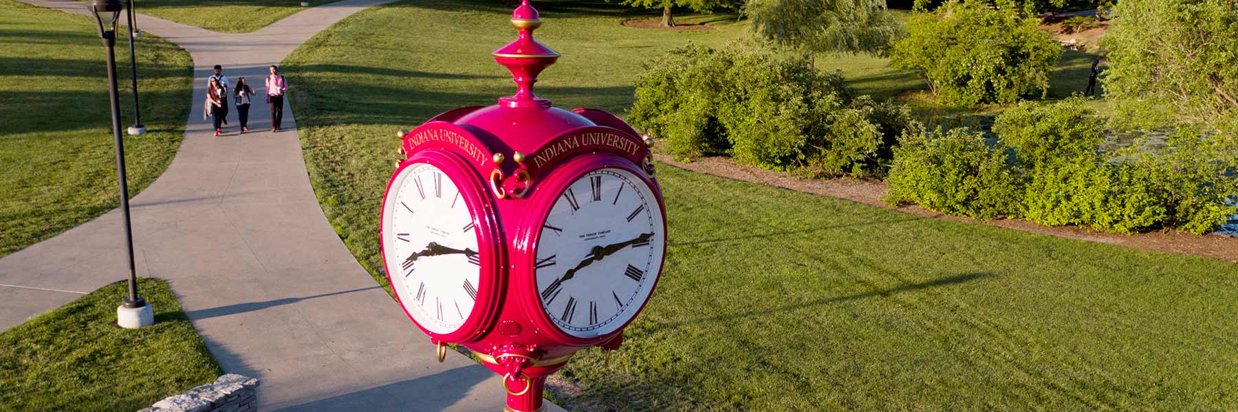 Decorative red clock on campus with students walking in background.